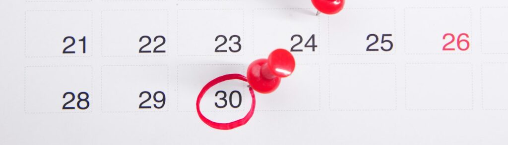 Calendário de mesa com alfinetes vermelhos marcando datas e o dia 30 circulado em vermelho