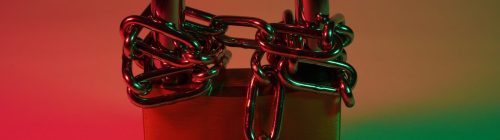 Cadeado vermelho preso por uma corrente de metal, com iluminação dramática vermelha e verde, representando um acesso bloqueado