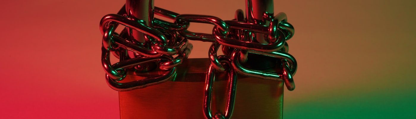 Cadeado vermelho preso por uma corrente de metal, com iluminação dramática vermelha e verde, representando um acesso bloqueado