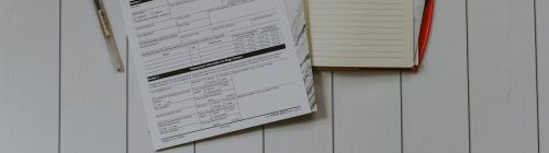 Formulário fiscal, caderno e caneta sobre mesa de madeira clara
